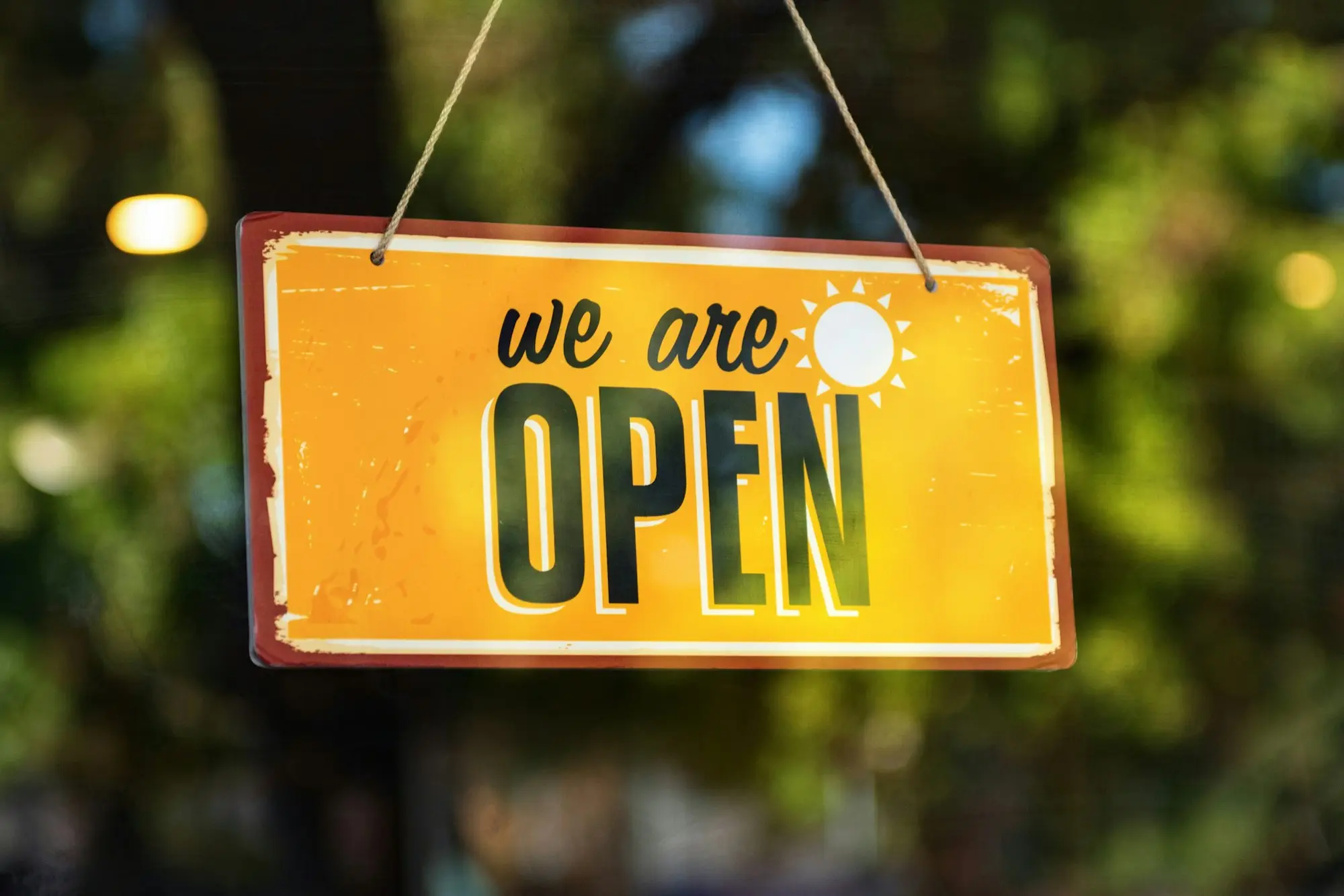 We are open sign hanging in a shop window in the morning light